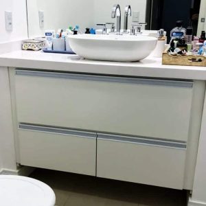 Gabinete de banheiro com porta basculante na parte de cima e duas gavetas na parte de baixo. Móvel branco produzido em MDF.